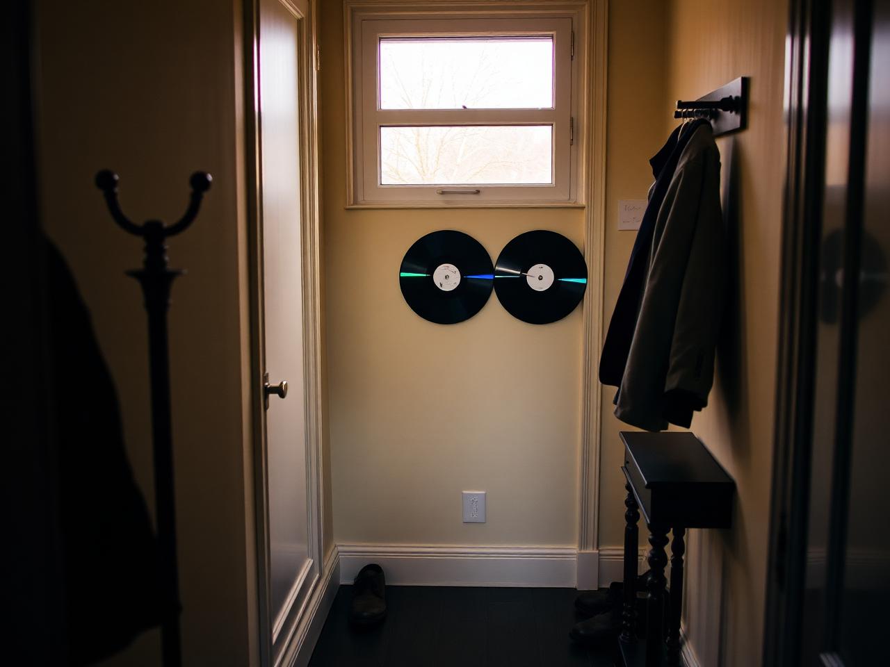 A narrow Utrecht townhouse hallway with a vertical triptych of three restored CDs beside the coat rack